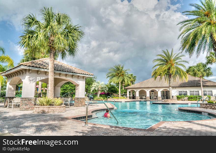 Outdoor resort swimming pool with palm trees on cloudy day.