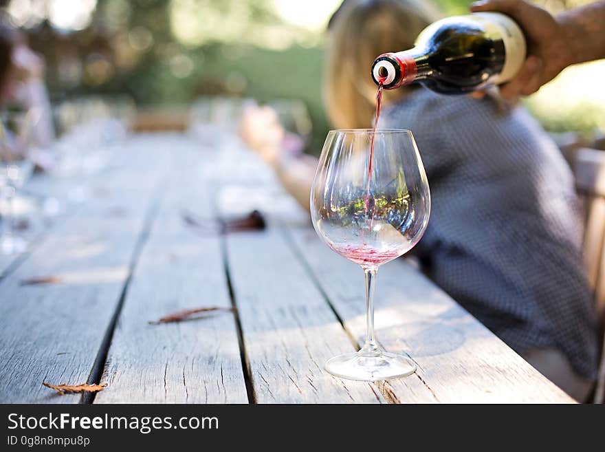 A person pouring red wine in a glass on desk with people in the background. A person pouring red wine in a glass on desk with people in the background.