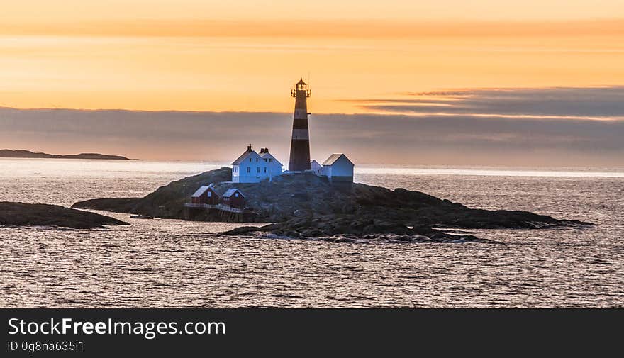 A lighthouse and a few houses on a small rocky island at sunset. A lighthouse and a few houses on a small rocky island at sunset.