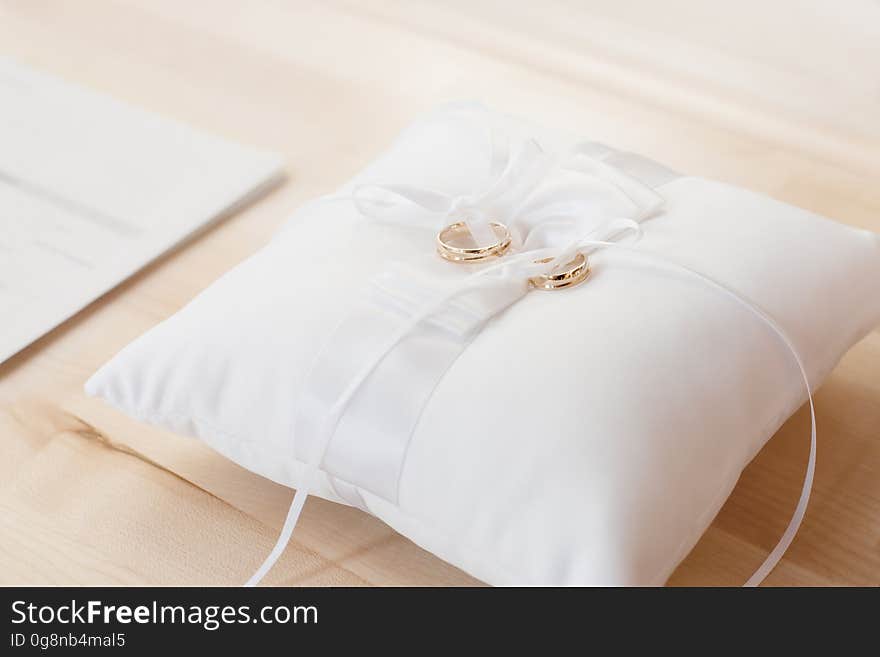 A white pillow with a ribbon and a pair of golden wedding rings on top. A white pillow with a ribbon and a pair of golden wedding rings on top.