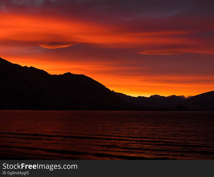 Magical orange and yellow sunset over the mountains with reflected glow on the waves in the sea (lake). Magical orange and yellow sunset over the mountains with reflected glow on the waves in the sea (lake).