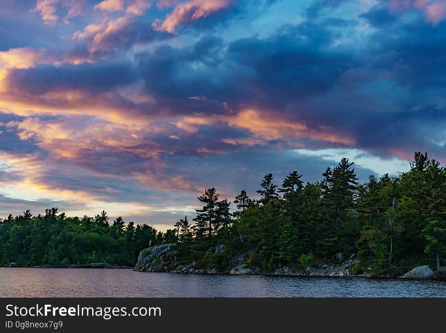 Scenic view of lake with forested coastline at dusk with dramatic cloudscape.