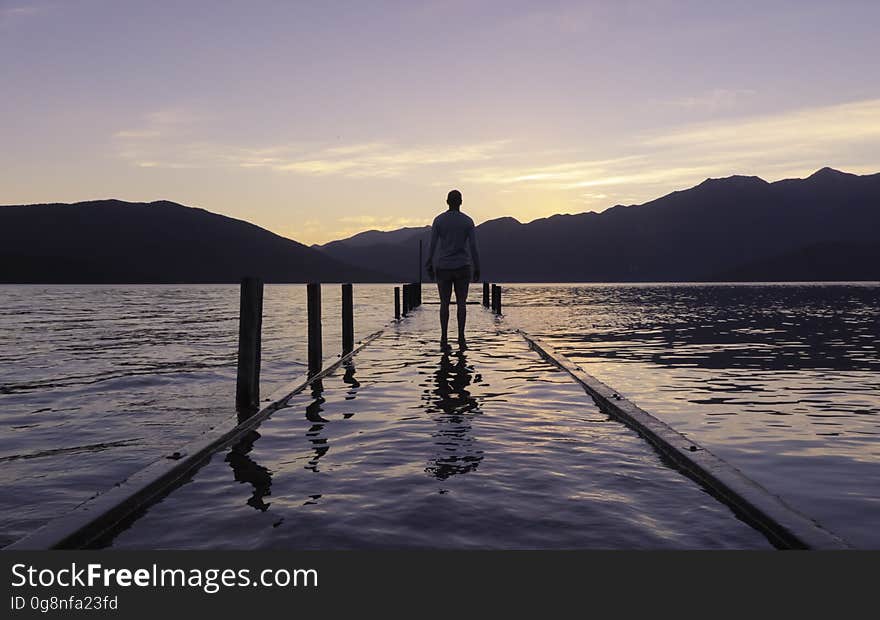 A person walking on a flooded pier at dusk. A person walking on a flooded pier at dusk.