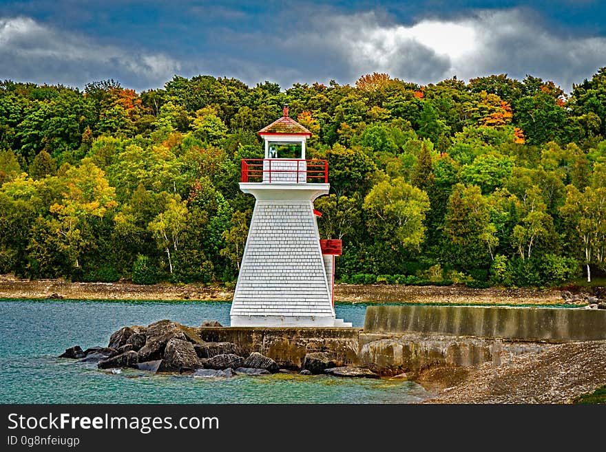 White lighthouse in front of a forest.