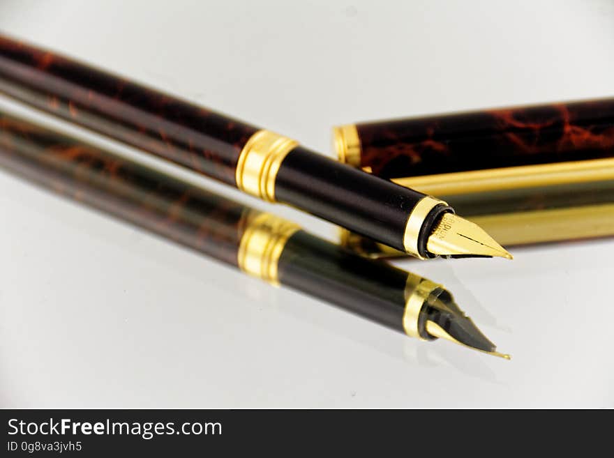 A close up of an elegant fountain pen reflecting on a glass surface. A close up of an elegant fountain pen reflecting on a glass surface.