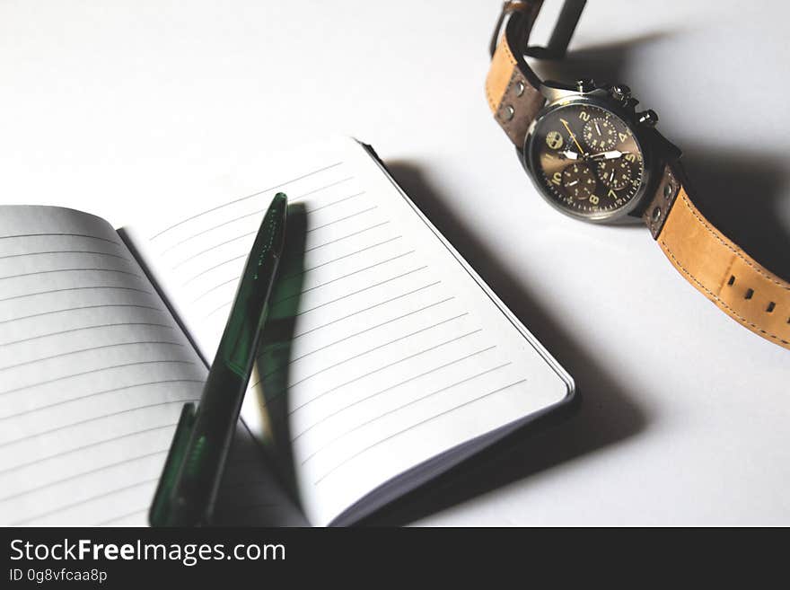 Pen on blank open pages of business notebook next to watch, white background. Pen on blank open pages of business notebook next to watch, white background.