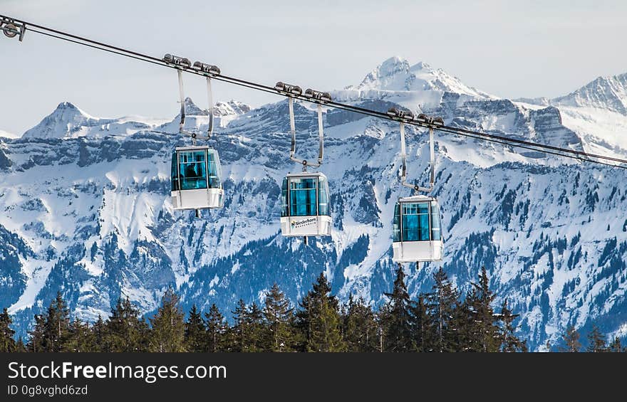 Alpine cable car over forest with snowy mountain range in background. Alpine cable car over forest with snowy mountain range in background.