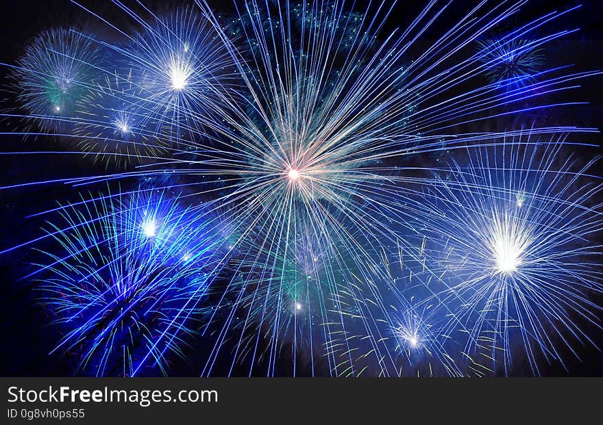 Fireworks exploding in sky with blue tone during New Years Eve display.