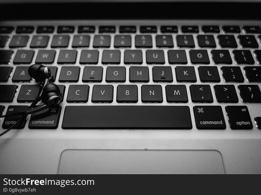 Black earphones resting on top of Apple Macbook keyboard. Black earphones resting on top of Apple Macbook keyboard.