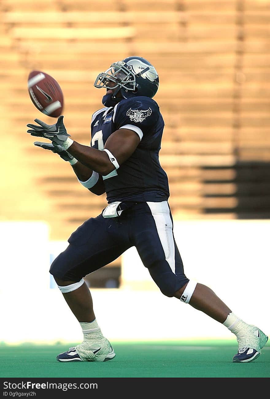 Football Player Wearing a Blue Jersey Catching a Football during Day Time