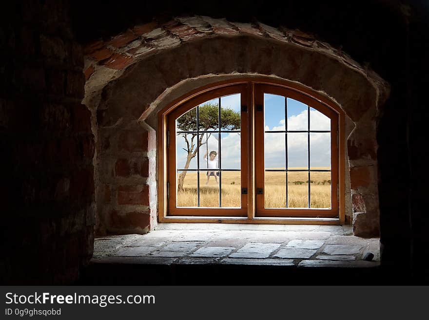 Interior view looking through window of old countryside building with child on swing under tree.