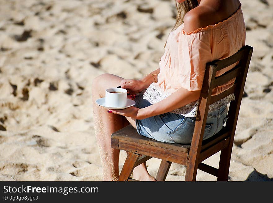 A woman sitting on a chair on a sandy beach with a coffee cup in hand. A woman sitting on a chair on a sandy beach with a coffee cup in hand.