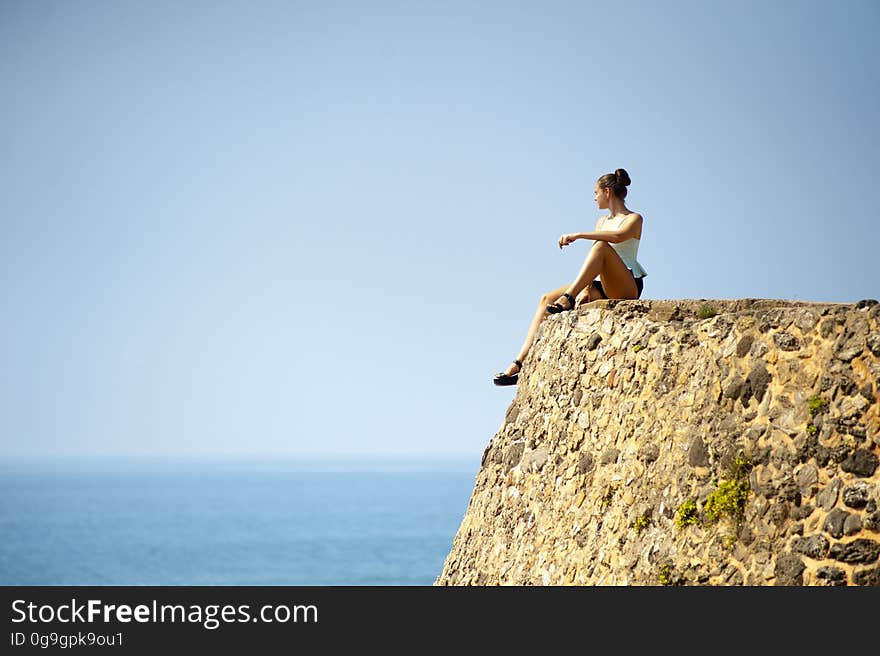 A young woman sitting on a rock by the sea looking at the horizon. A young woman sitting on a rock by the sea looking at the horizon.