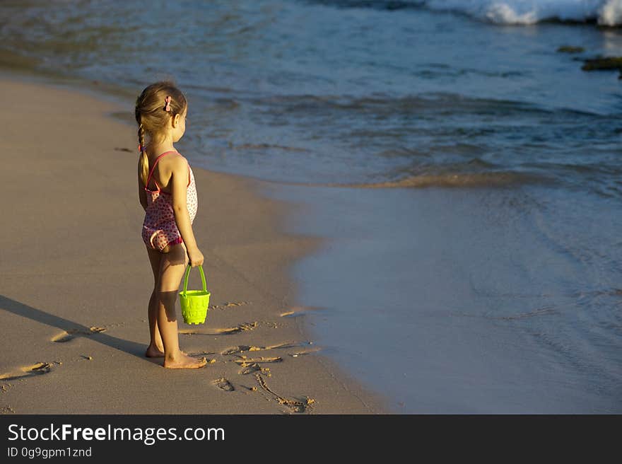 A young girl standing on the beach with a plastic pail in hand. A young girl standing on the beach with a plastic pail in hand.