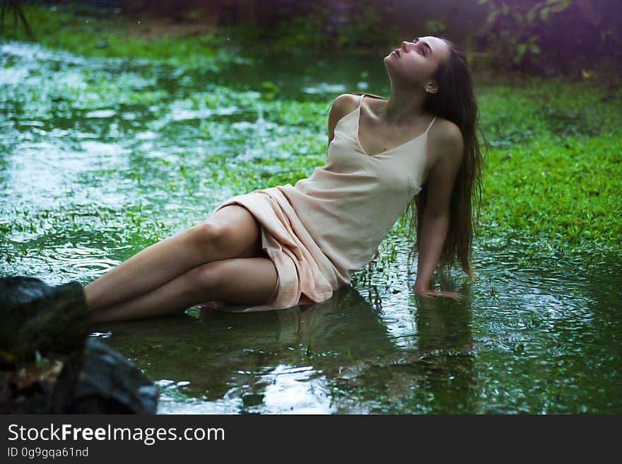 Thoughtful young woman in pink silk nighty half lying, half sitting in a wet muddy field. Thoughtful young woman in pink silk nighty half lying, half sitting in a wet muddy field.