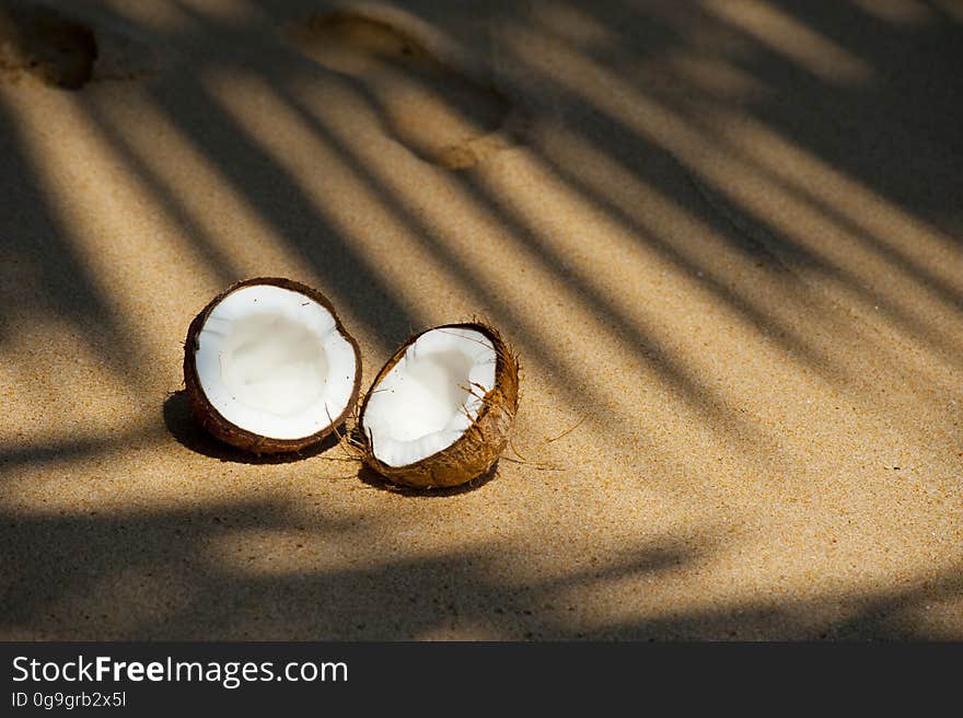 A coconut broken in two halves on a sandy beach. A coconut broken in two halves on a sandy beach.