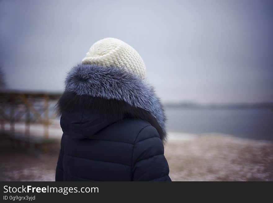 A woman wearing a beanie and a jacket wit fur-rimmed hood standing on the beach in the winter. A woman wearing a beanie and a jacket wit fur-rimmed hood standing on the beach in the winter.