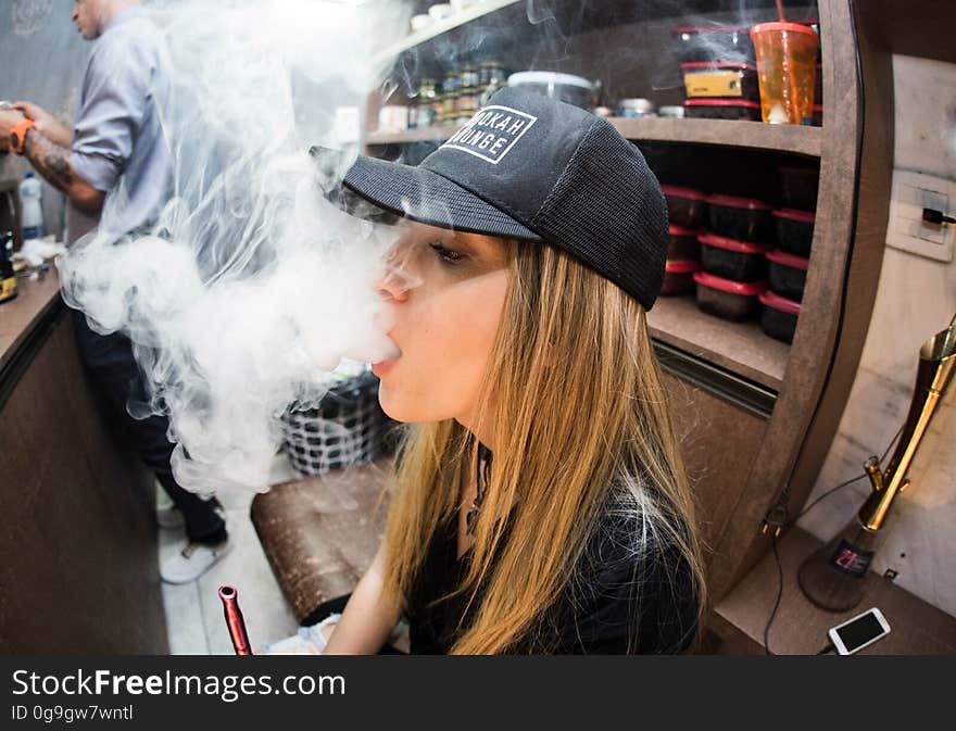 Trendy young woman vaping in restaurant with cloud of vapor.