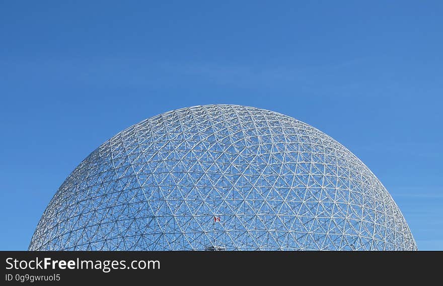 Exterior of futuristic domed glass building with blue sky background.