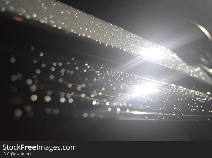 Monochrome view of light glistening off dew drops on smooth surface.