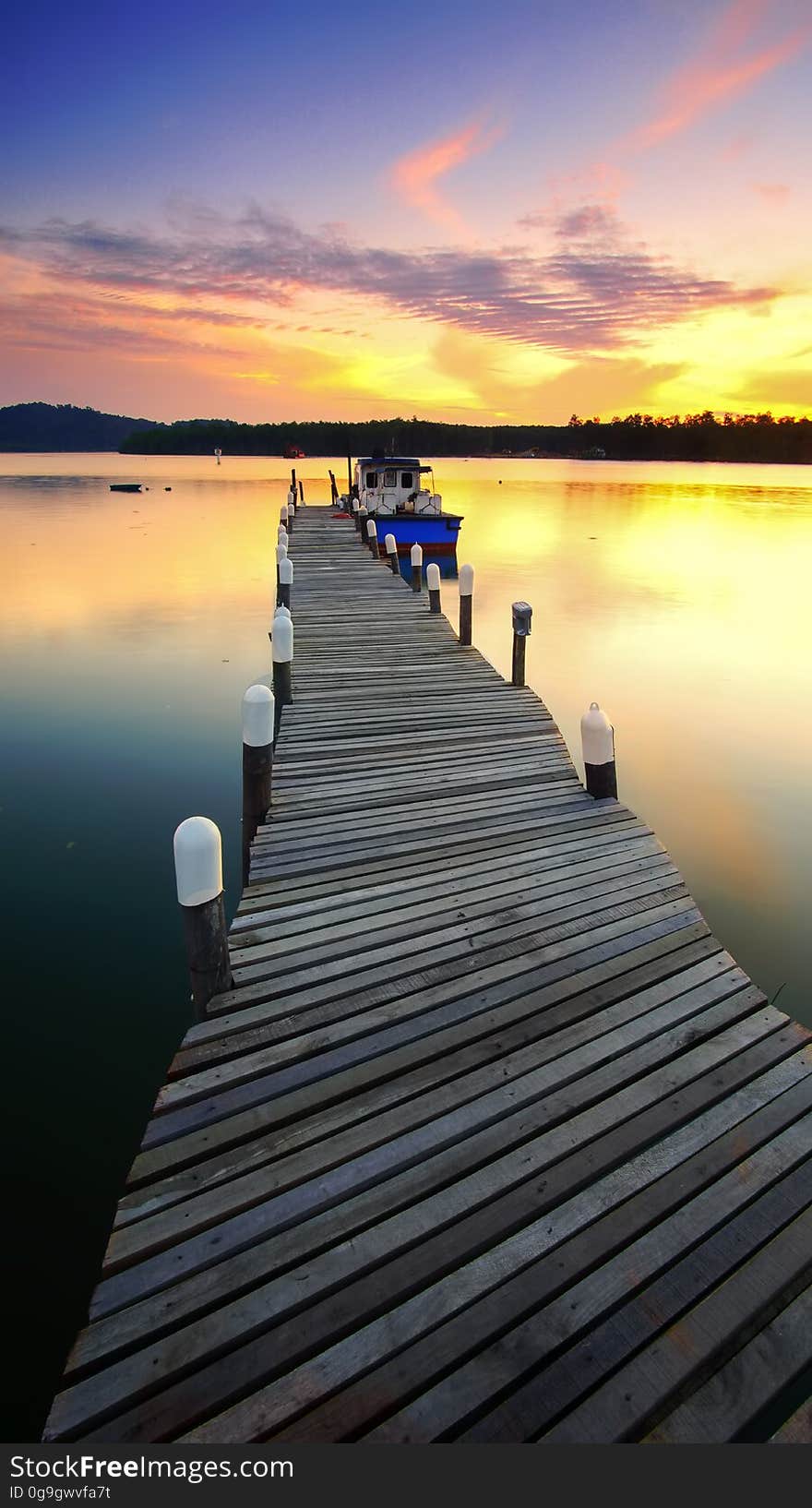 Boat moored at end of long wooden jetty on lake at sunset. Boat moored at end of long wooden jetty on lake at sunset.