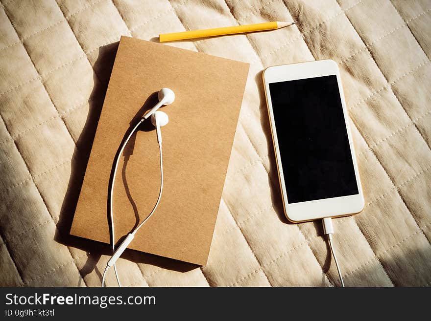 A notebook and a smartphone with a headset on a fabric background. A notebook and a smartphone with a headset on a fabric background.