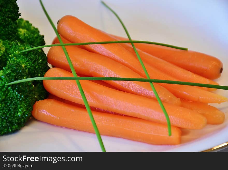 A plate with blanched carrots and broccoli with chives on top.