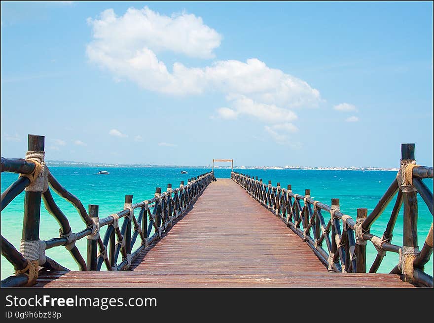 Long wooden jetty with decorative railings to left and right poking out into an aquamarine sea, pale blue sky with light clouds. Long wooden jetty with decorative railings to left and right poking out into an aquamarine sea, pale blue sky with light clouds.