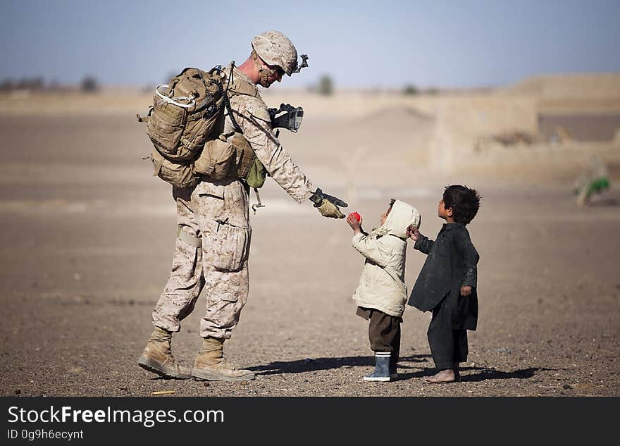 Soldier Giving Red Fruit on 2 Children during Daytime