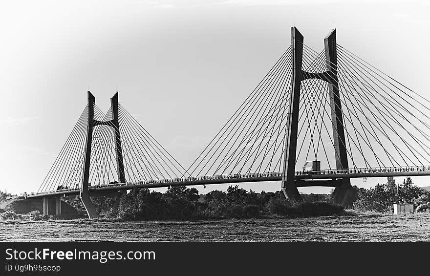 Suspension bridge across a river showing supporting cables and two towers, urban conurbation and trees are seen in silhouette..