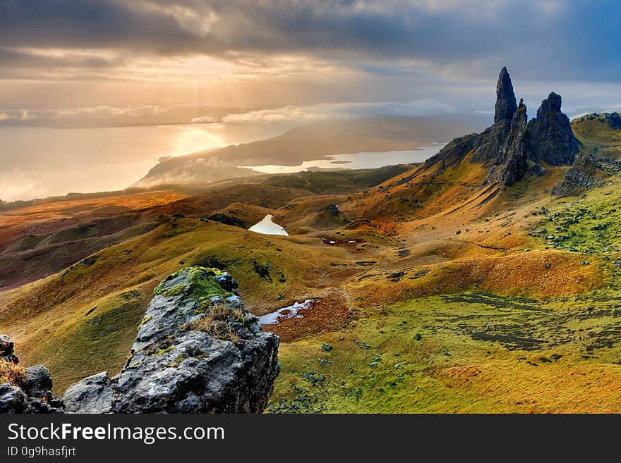 Rolling landscape with Autumn colors, shades of green and orange, with needle like rocks, pale blue lake, and blue gray sky. Rolling landscape with Autumn colors, shades of green and orange, with needle like rocks, pale blue lake, and blue gray sky.