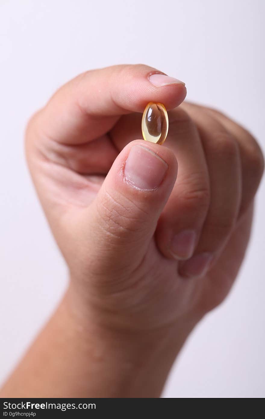 Closeup of hand with capsule held between thumb and forefinger, white background. Closeup of hand with capsule held between thumb and forefinger, white background.