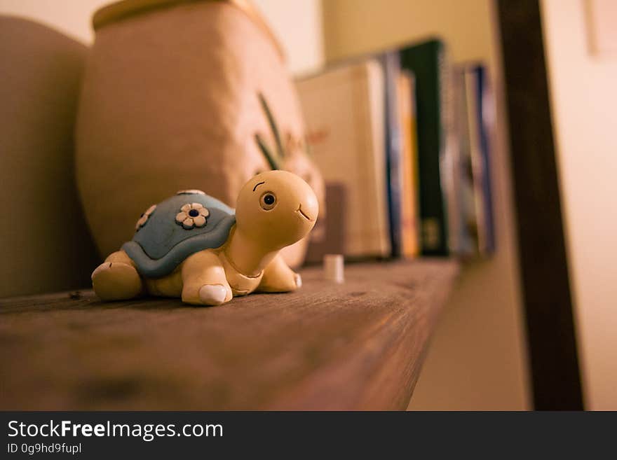 A clay turtle toy on a shelf with books and pots. A clay turtle toy on a shelf with books and pots.