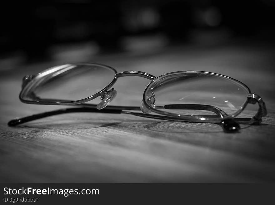 A black and white image of eyeglasses on a wooden desk. A black and white image of eyeglasses on a wooden desk.