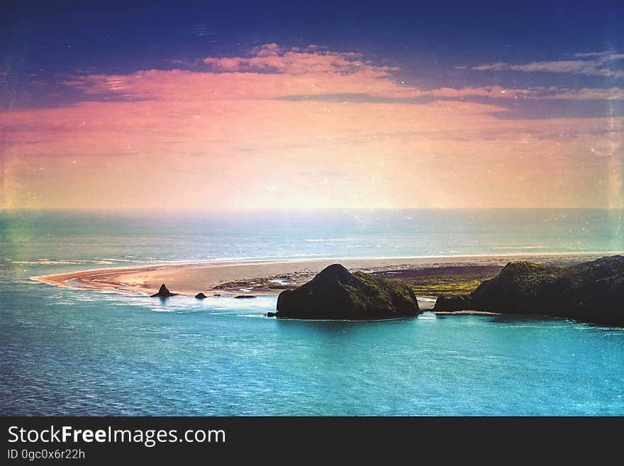 Green Island Surrounded by Blue Ocean Under Blue and Orange Sky