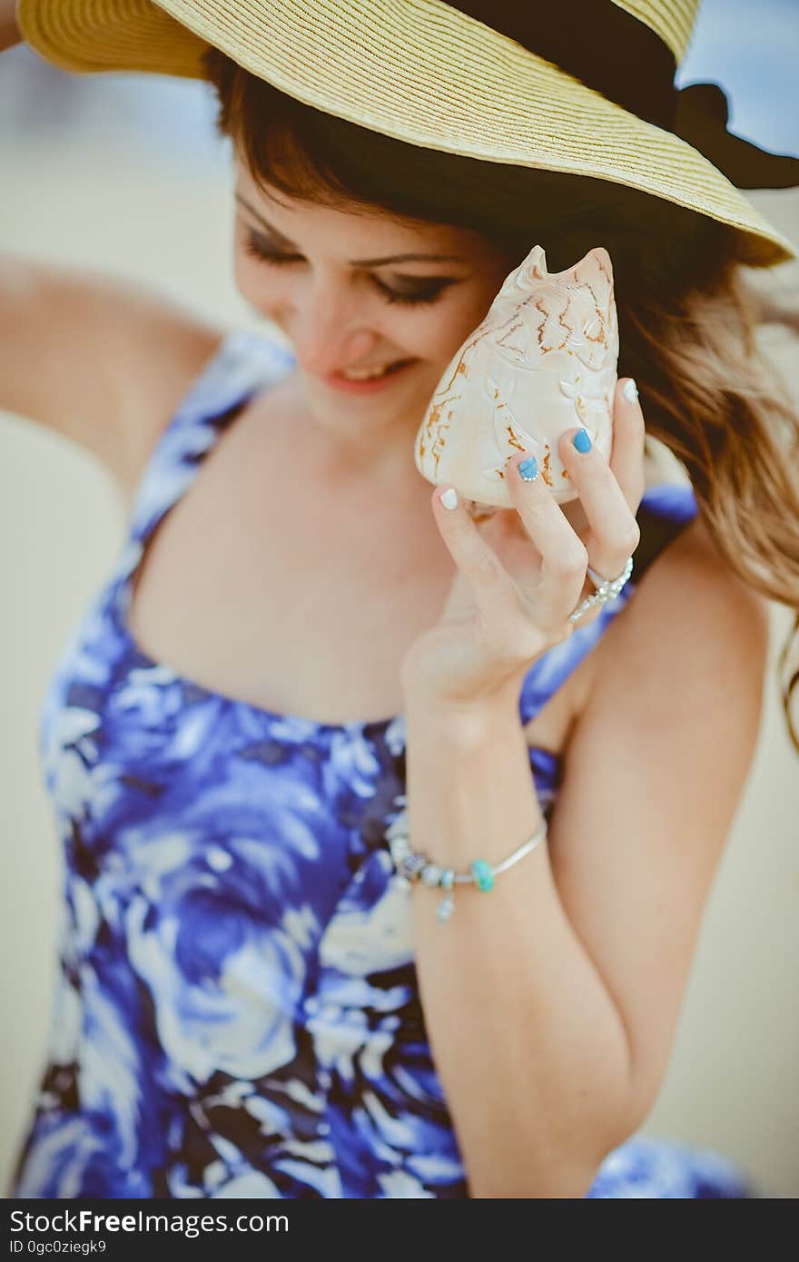 A young woman at the beach listening to a shell.