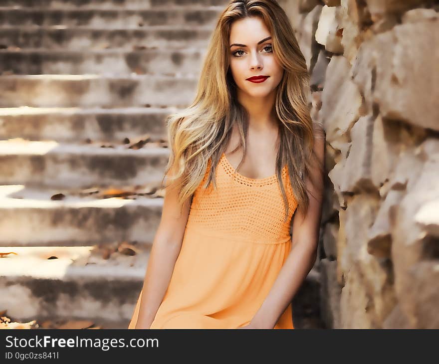 A young woman with long hair leaning on a stone wall. A young woman with long hair leaning on a stone wall.