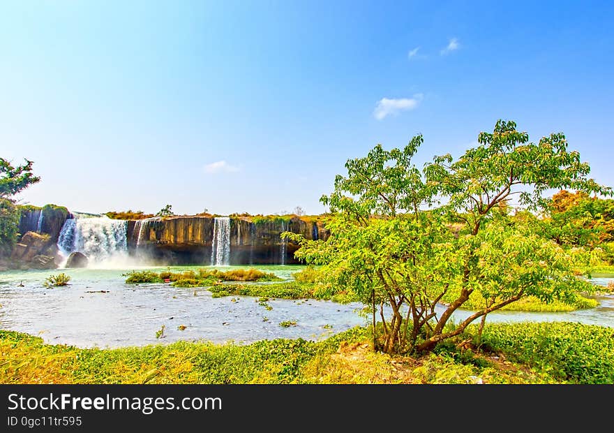 Scenic view of waterfall in green countryside with trees in foreground. Scenic view of waterfall in green countryside with trees in foreground.