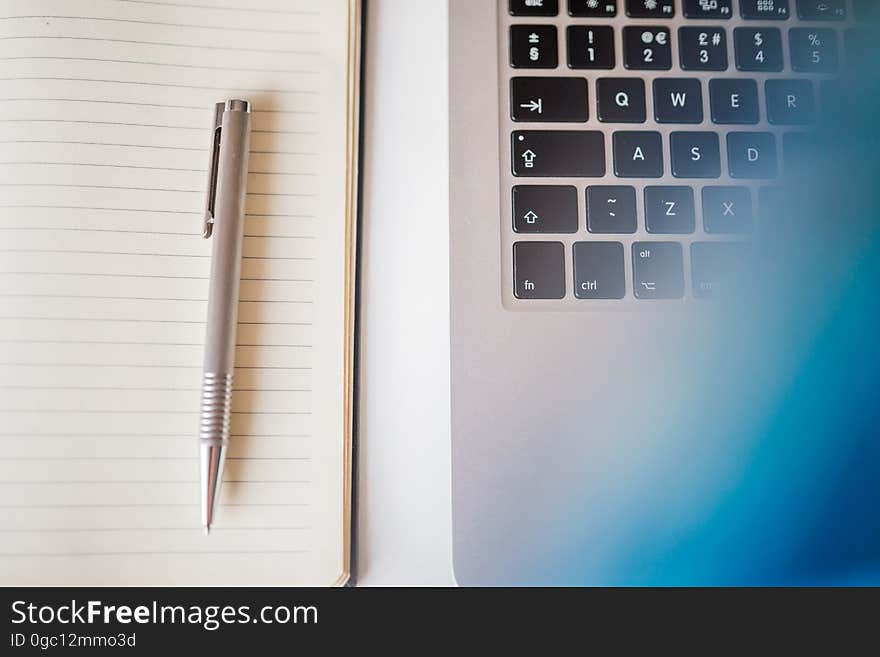 Grey Pen in White Lined Paper Beside Grey Laptop Computer