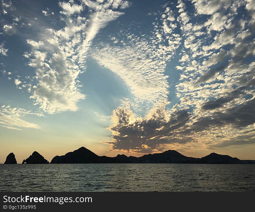 A sea view with colorful sunset and clouds over mountains in the horizon. A sea view with colorful sunset and clouds over mountains in the horizon.