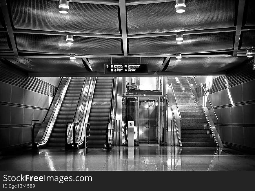 A transit hub or terminal with escalators and stairs in black and white.