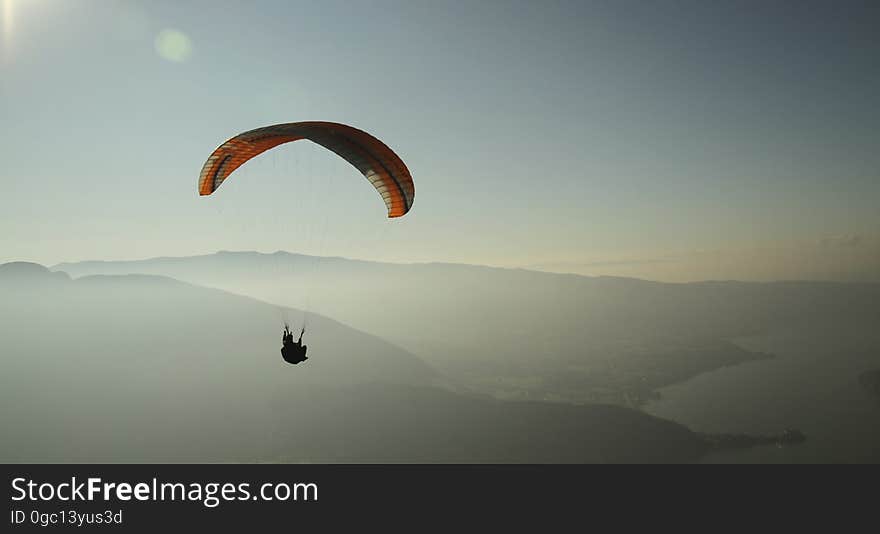 A parachutist sailing in the air over mountains and water. A parachutist sailing in the air over mountains and water.