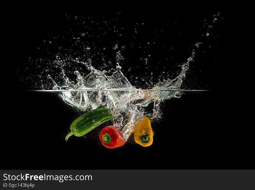 A trio of colorful peppers falling in water on black background. A trio of colorful peppers falling in water on black background.