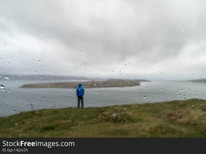 Distant shot of the back of a man standing on the shore by water on a cloudy, foggy day. Focus of photo is mist on lens of the camera with shallow depth of field. Distant shot of the back of a man standing on the shore by water on a cloudy, foggy day. Focus of photo is mist on lens of the camera with shallow depth of field.