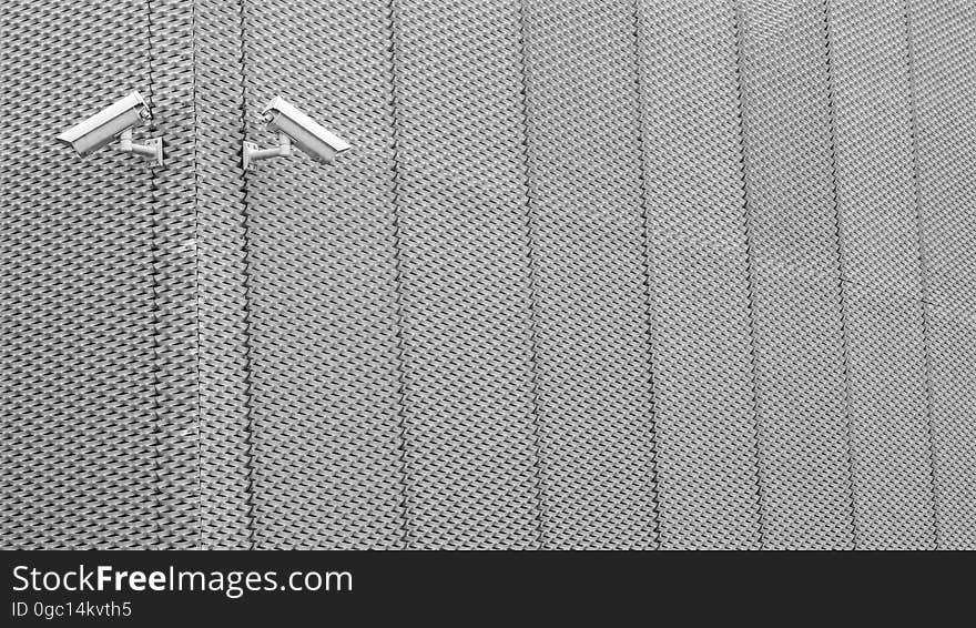 Security surveillance cameras on exterior aluminum fence in daylight. Security surveillance cameras on exterior aluminum fence in daylight.