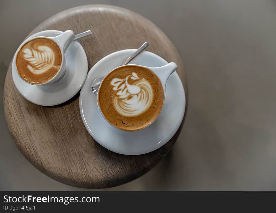 Overhead view of cups with coffee latte on saucers with spoons on wooden board. Overhead view of cups with coffee latte on saucers with spoons on wooden board.