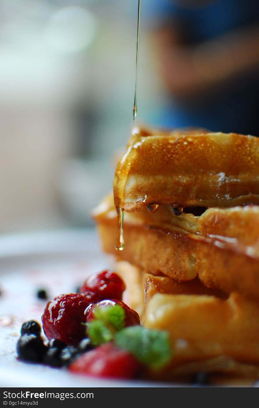 Syrup pouring on close up of stack of waffles with fresh fruit on plate. Syrup pouring on close up of stack of waffles with fresh fruit on plate.