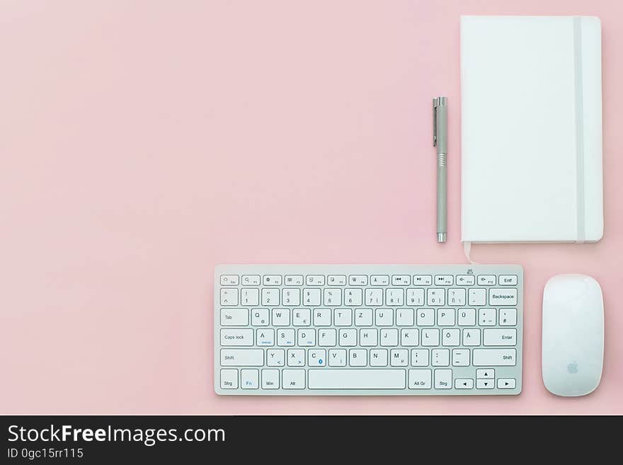 Keyboard and mouse with Apple logo on pink background with blank notepaper and pen. Keyboard and mouse with Apple logo on pink background with blank notepaper and pen.