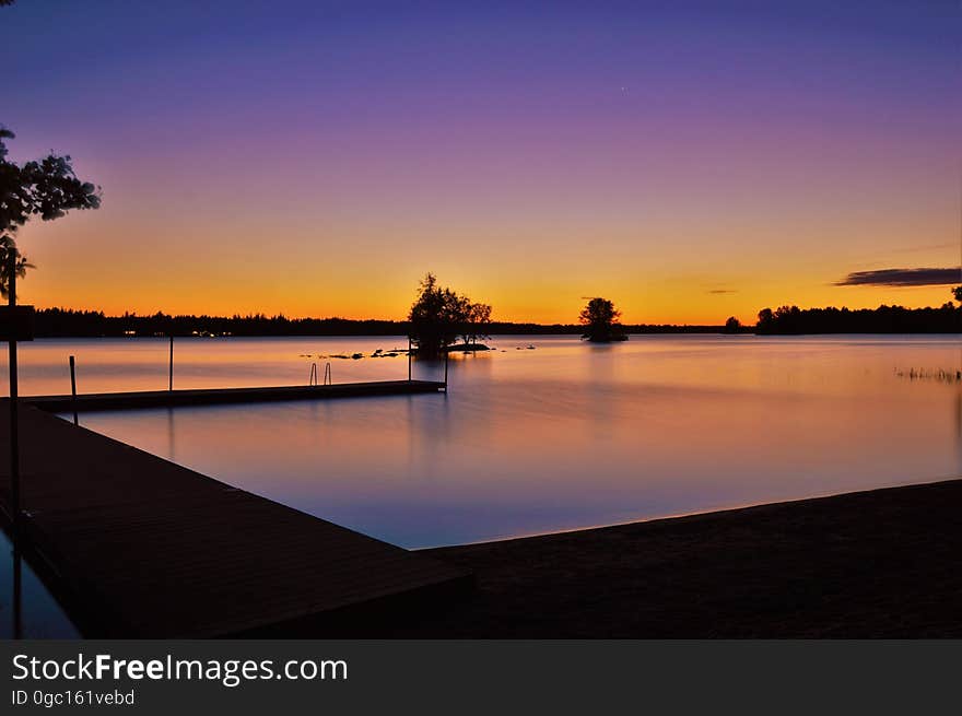 Sunset over river waterfront with silhouette of trees.