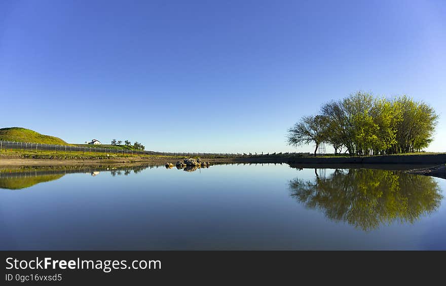 Rural landscape with reflection on tree on banks of clear blue waters on sunny day. Rural landscape with reflection on tree on banks of clear blue waters on sunny day.